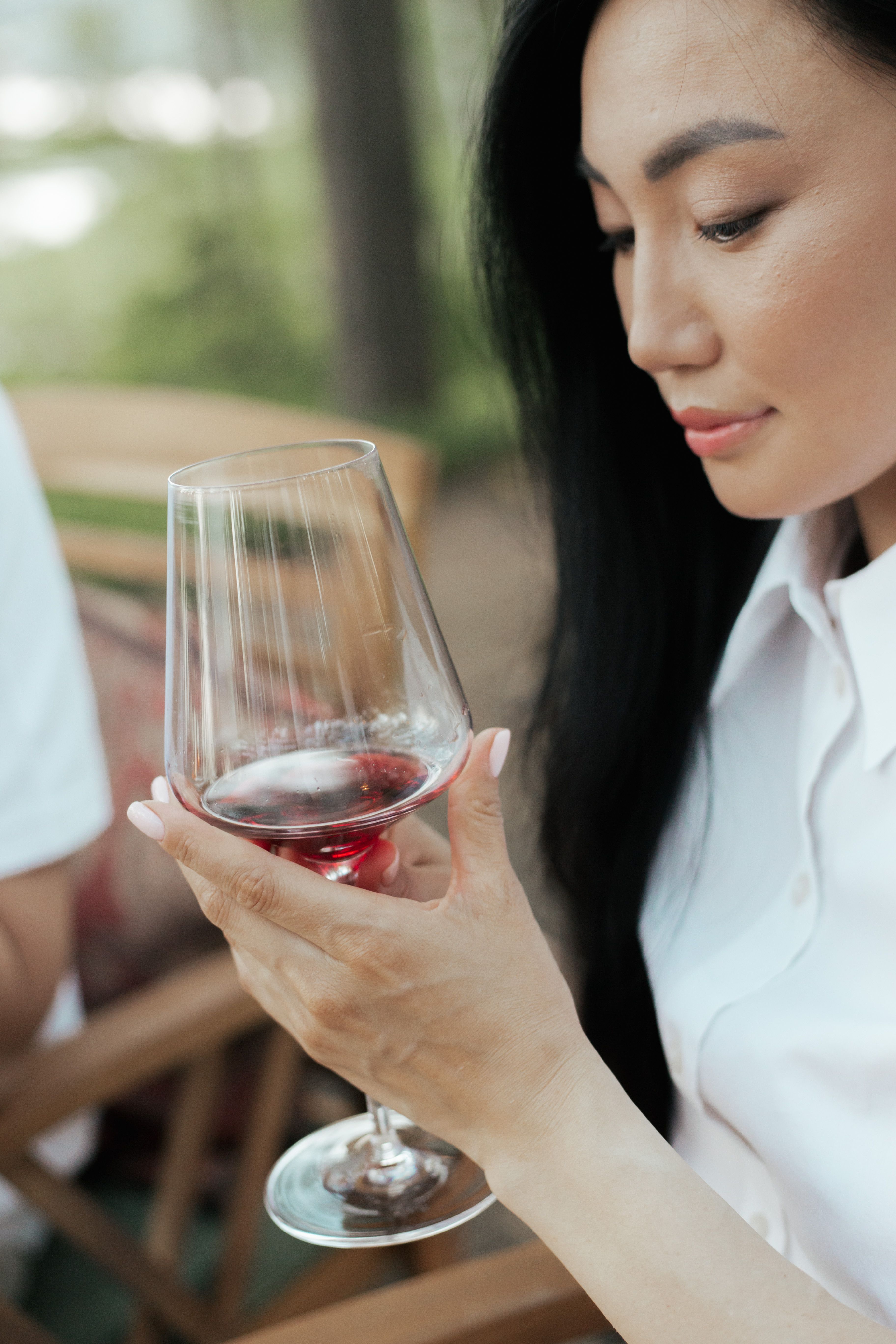 A woman studying a glass of red wine carefully at an outdoor table, evocative of a winemaker at work