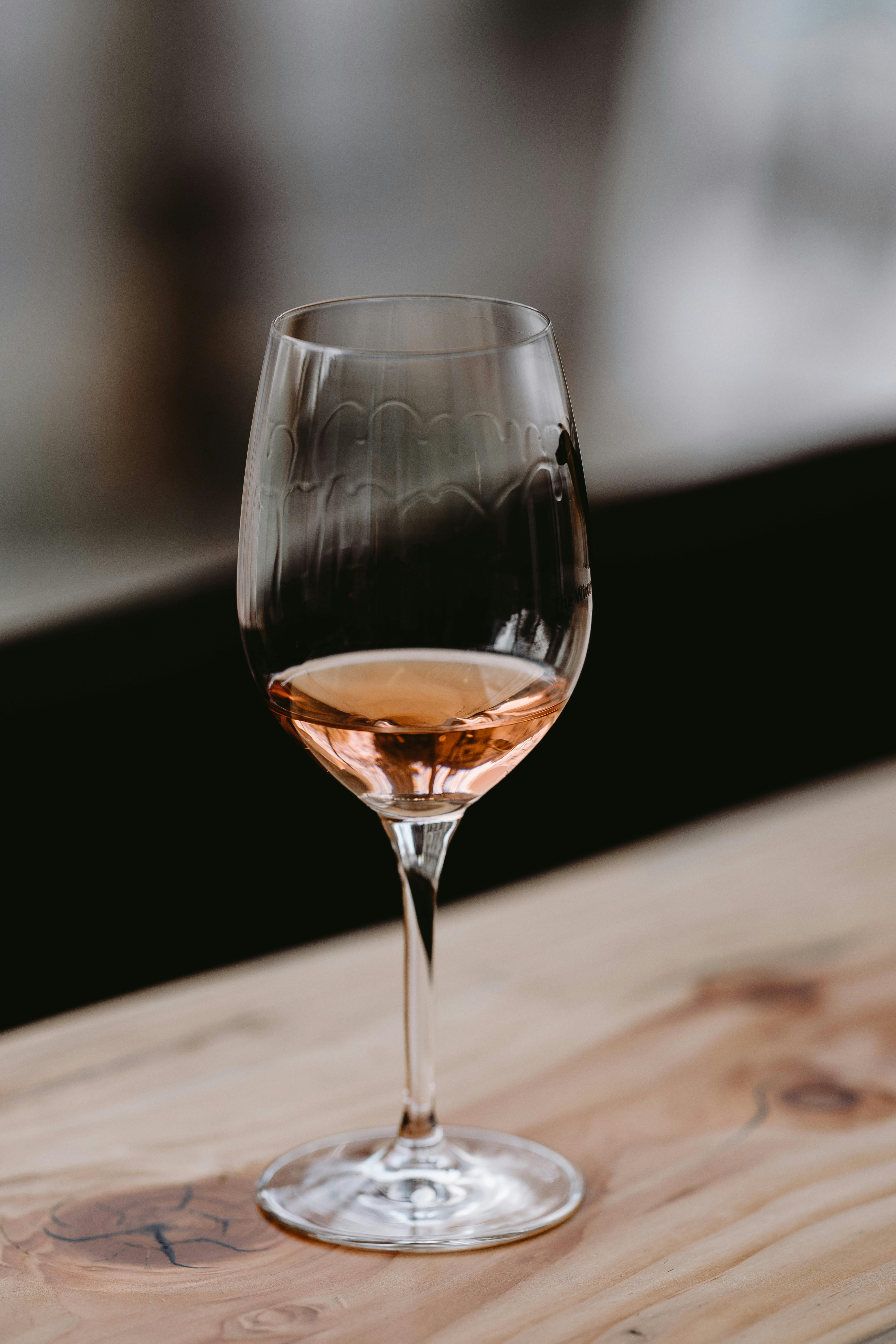 A glass of rosé wine resting on a wooden surface, lit by warm afternoon light